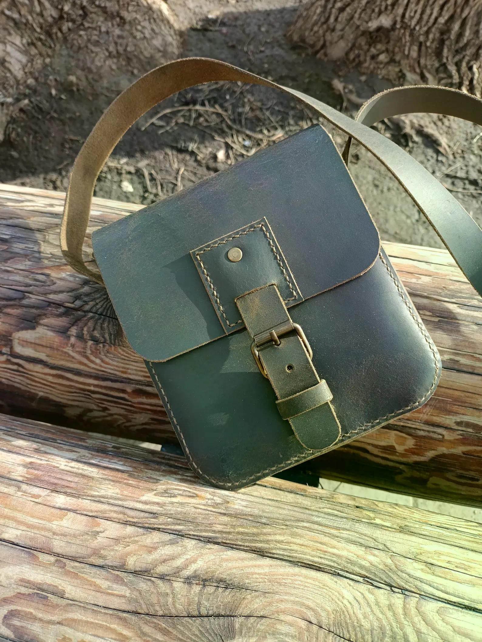 Handmade gray leather messenger bag with a flap and shoulder strap displayed outdoors