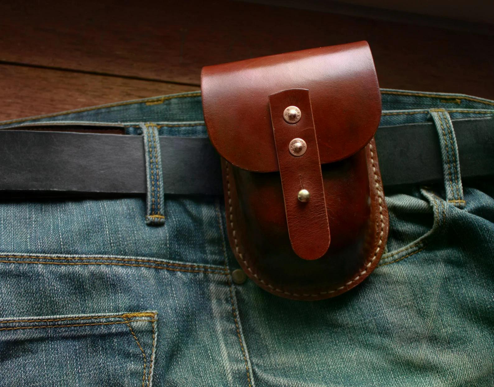 Handmade brown leather belt pouch attached to a belt over denim jeans