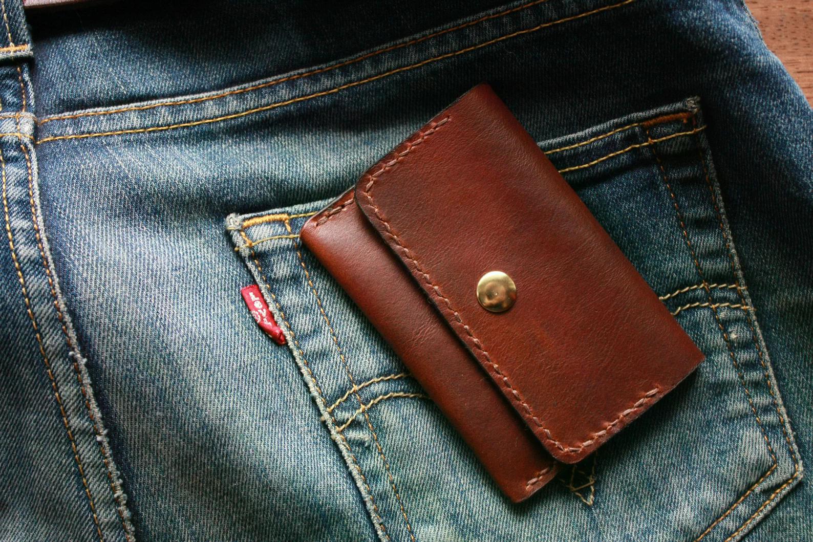 Hand sewn brown leather wallet and coin holder resting on denim fabric
